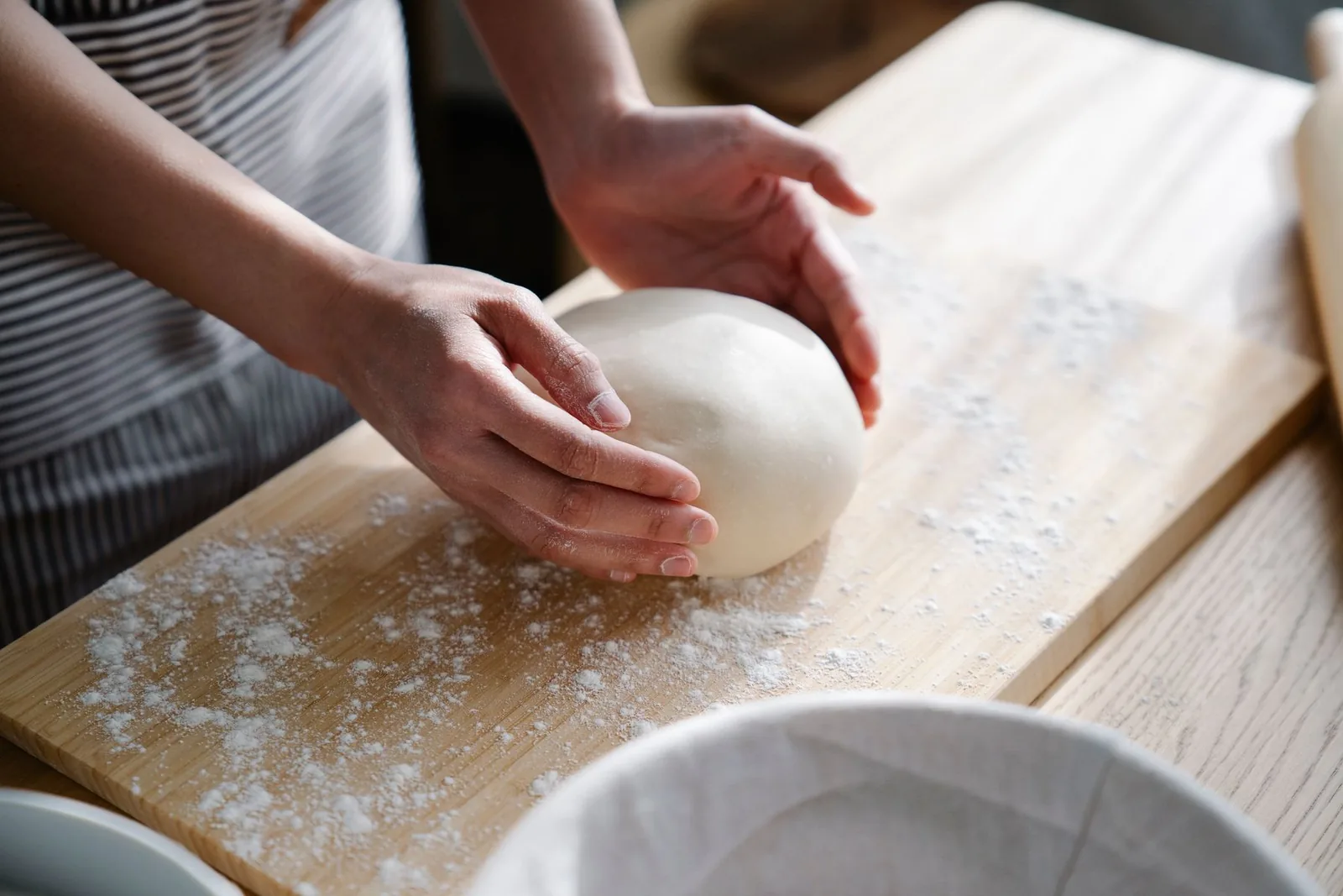 Des mains pétrissent une pâte sur une planche.