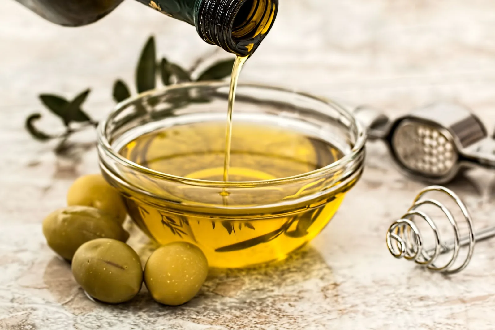 De l’huile d’olive versée dans un bol en verre à côté d’olives.